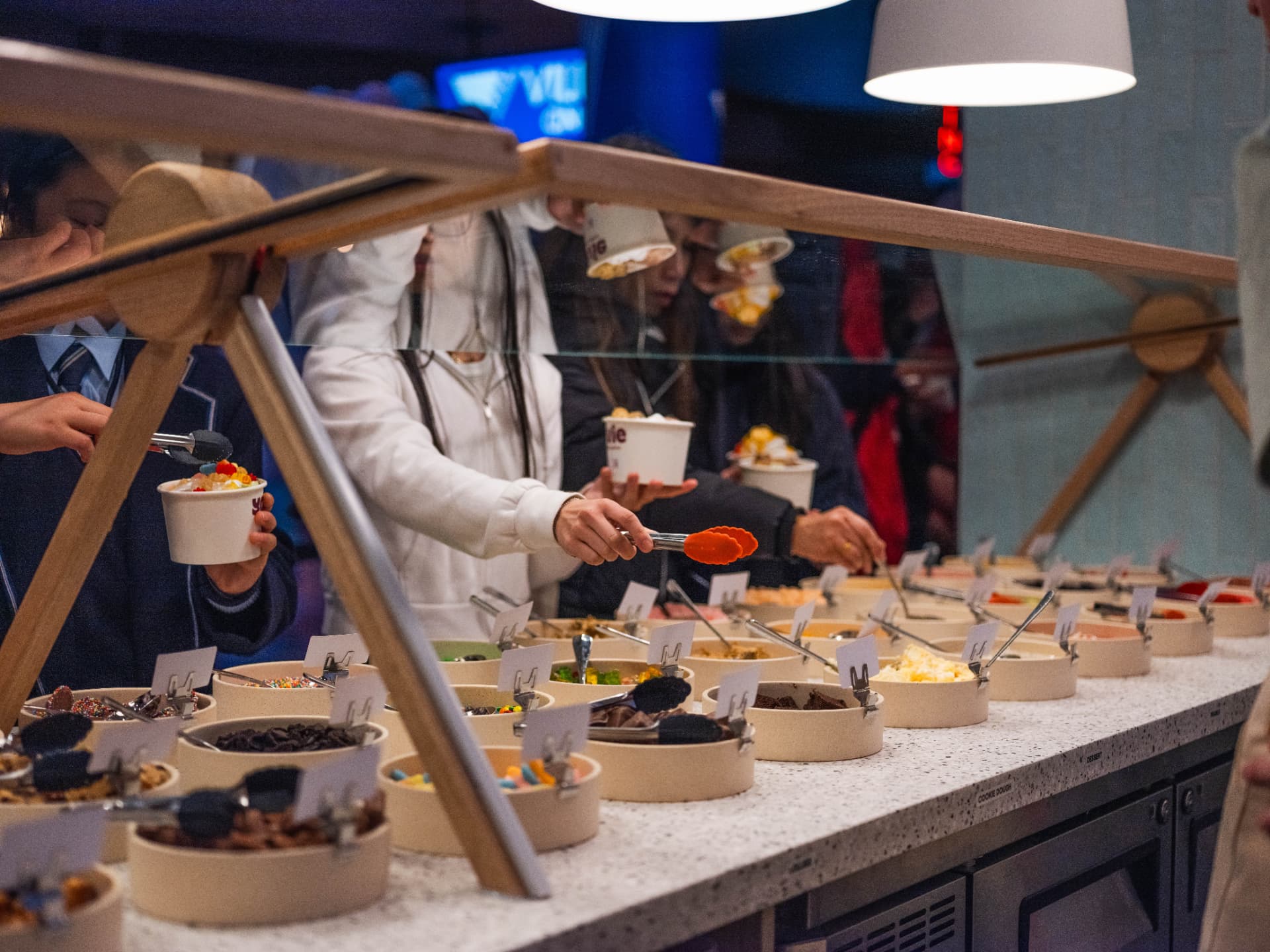 Customers using tongs to add toppings at the YOVIE self-serve topping bar