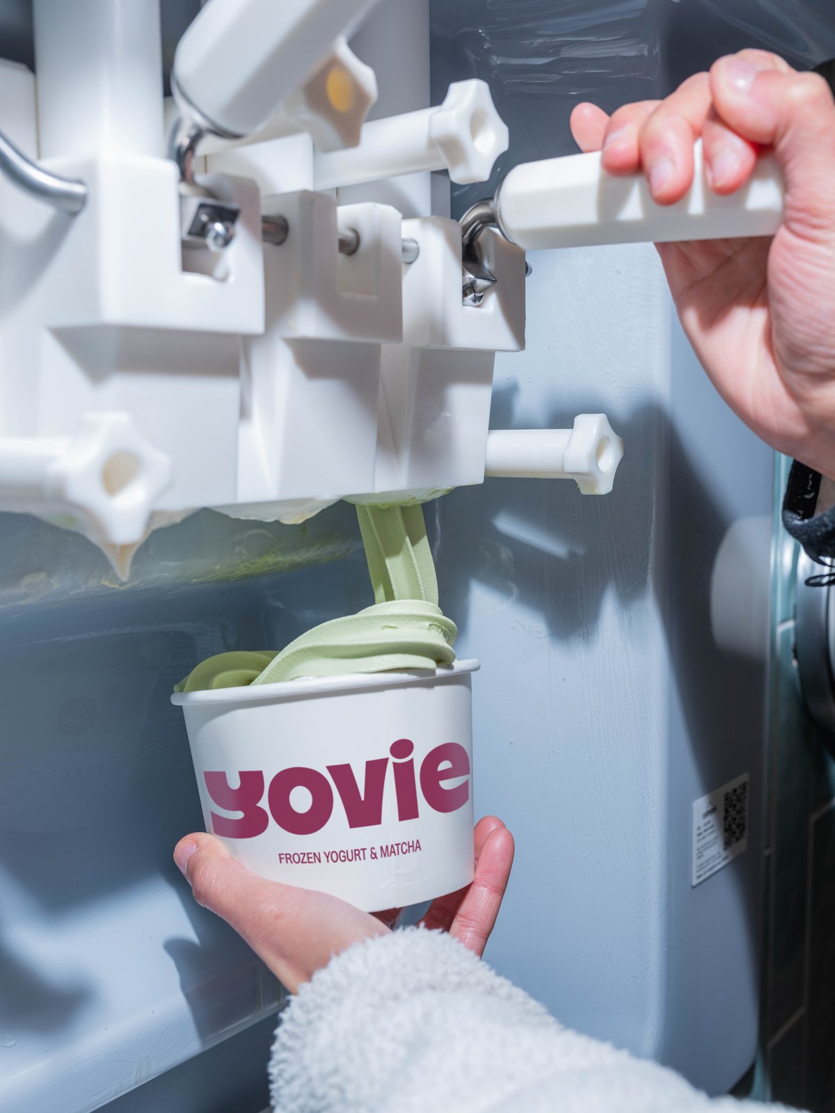 Matcha frozen yogurt being served into a YOVIE cup at a self-serve machine