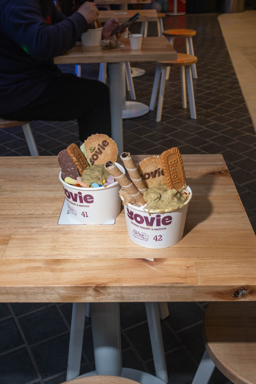Two YOVIE frozen yogurt cups with toppings on a table in the seating area