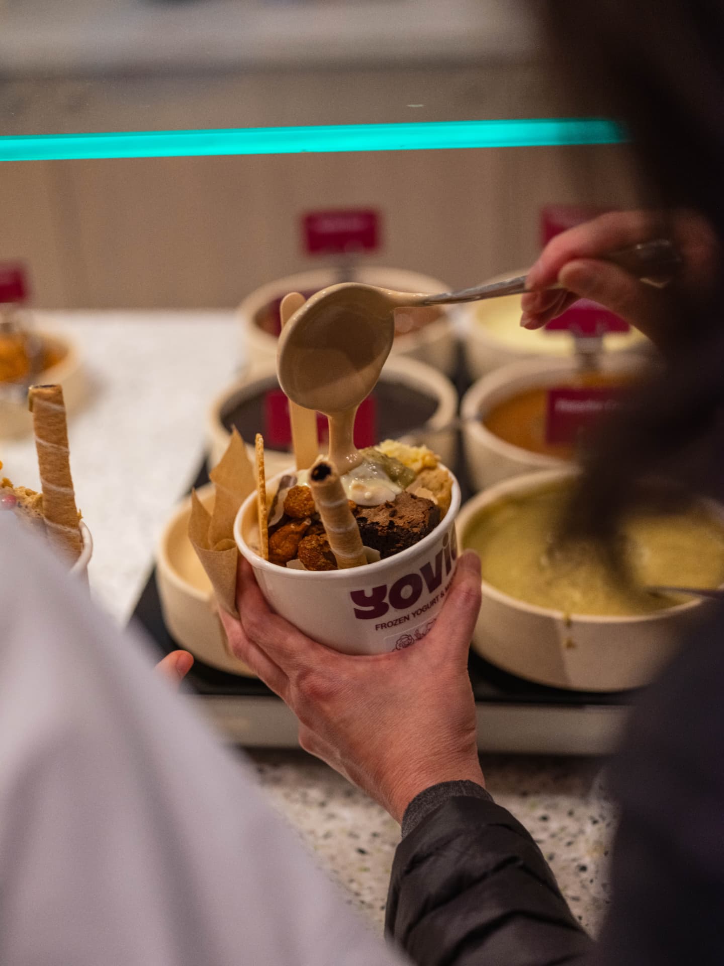 A customer adding toppings to a YOVIE frozen yogurt cup at the self-serve topping bar